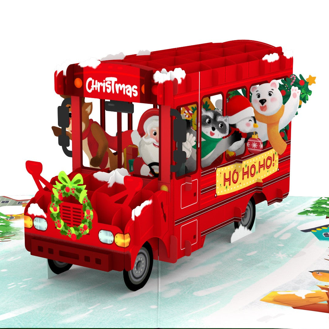 A 3D pop-up book illustration featuring a red Christmas bus filled with festive characters, set against a snowy winter landscape on an open pop up card.