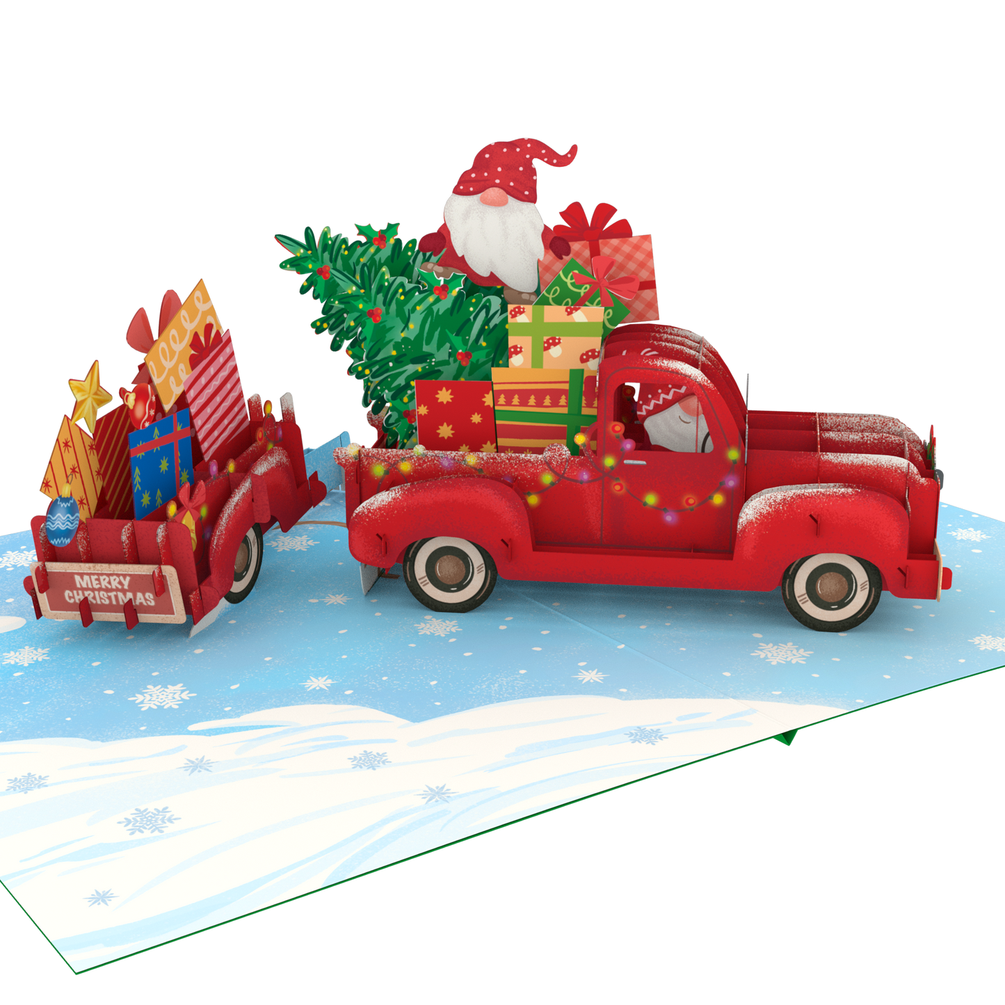 A 3D pop-up cardboard Christmas gift truck scene on a snowy blue ground. A red pickup truck carries a green Christmas tree and wrapped presents, with Santa Claus visible in the driver's seat.