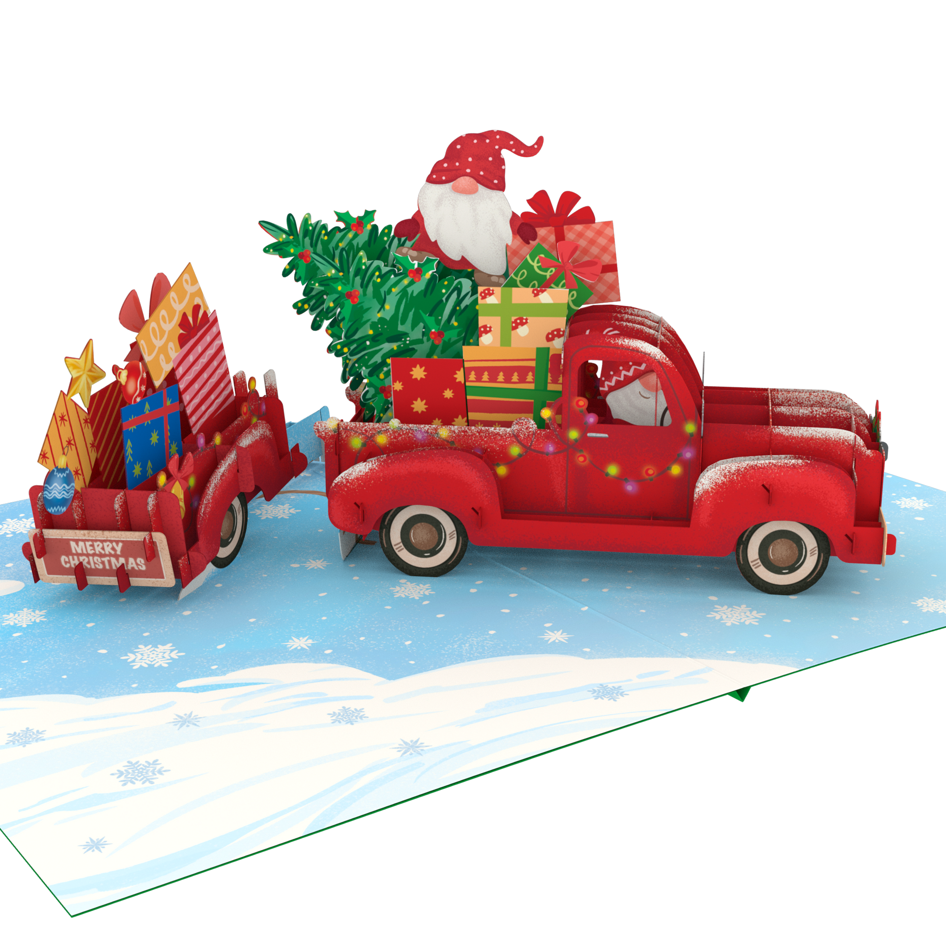 A 3D pop-up cardboard Christmas gift truck scene on a snowy blue ground. A red pickup truck carries a green Christmas tree and wrapped presents, with Santa Claus visible in the driver's seat.