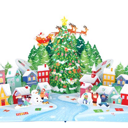 A colorful 3D pop-up cardboard Christmas village scene with a decorated Christmas tree, Santa in a sleigh, houses, snow, children, and a winding blue river on a white background.