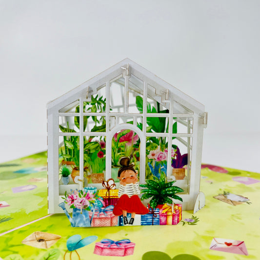 A greeting card depicting a three-dimensional scene with a little girl sitting outside a garden house surrounded by colorful gift boxes and plants.