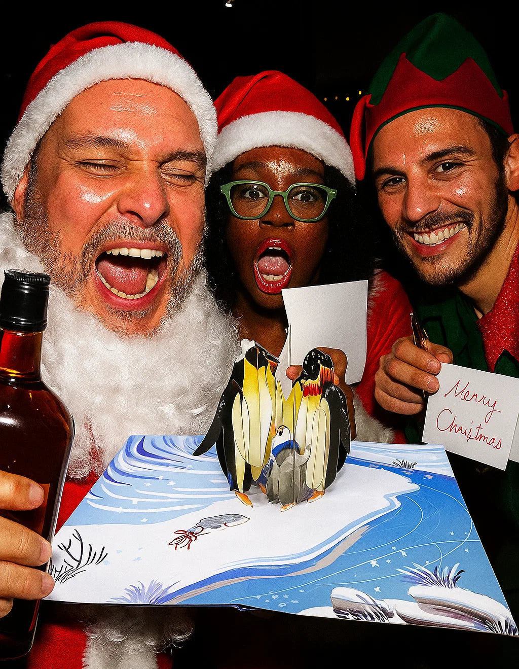 Three people in festive attire with a Christmas card featuring penguins.