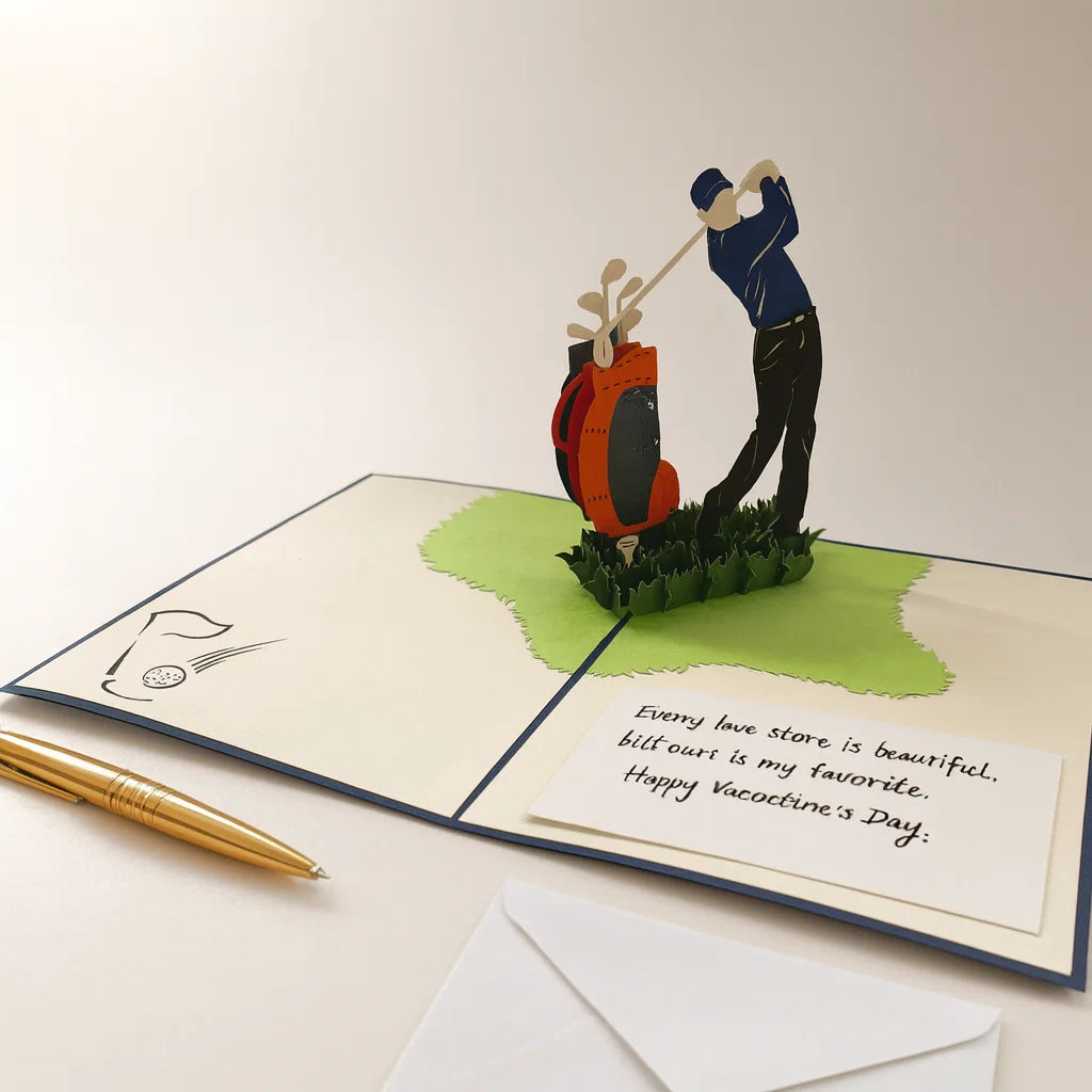 Greeting card with 3D pop-up design of a golfer and golf bag, with a pen and envelope on a light background.