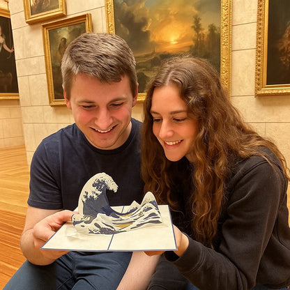 Two people holding a 3D printed model of a wave in a room with framed paintings on the wall.