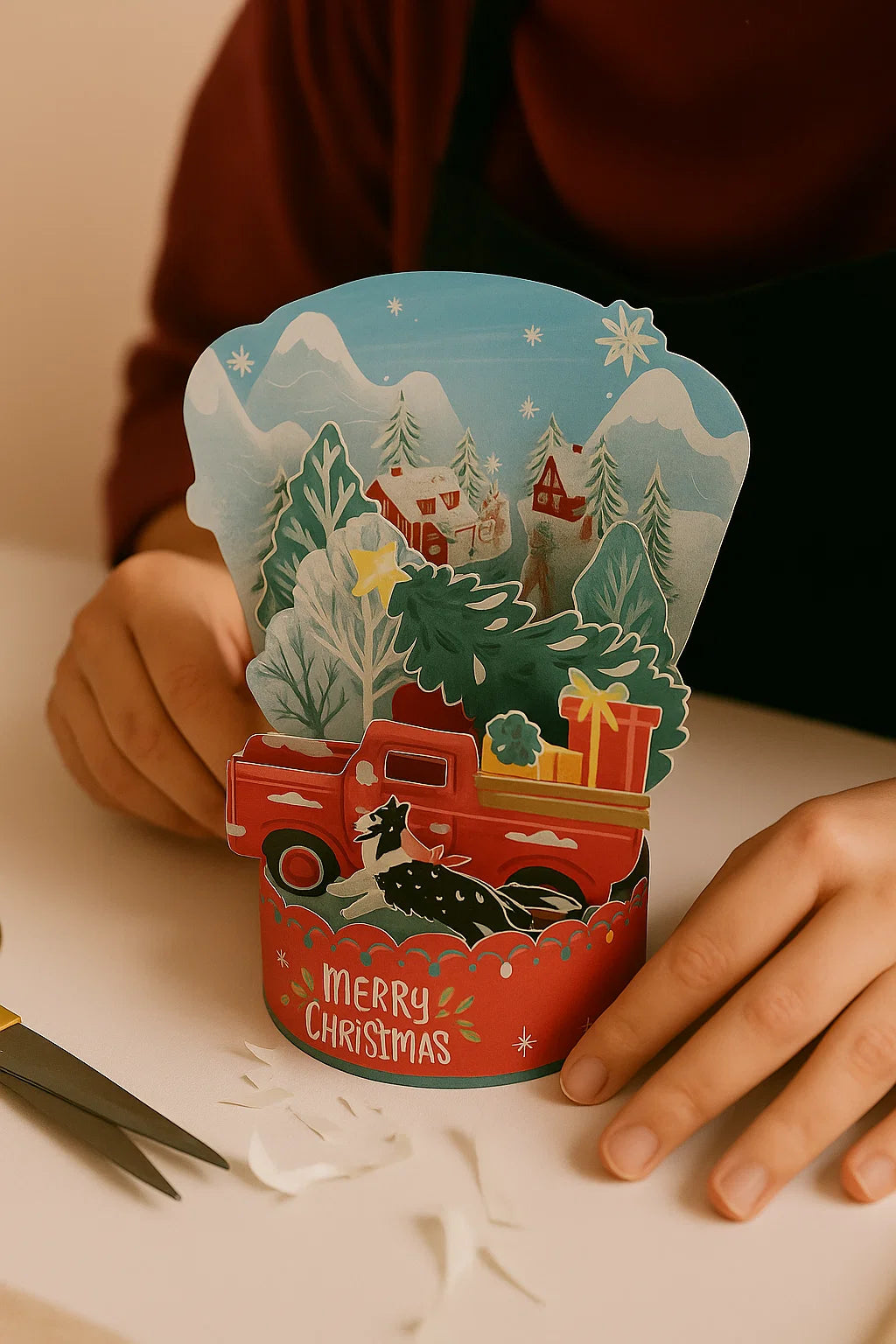 Hand holding a Christmas-themed pop-up card with a red truck and snowy landscape.