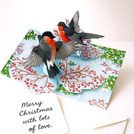 Christmas card with two birds on a snowy branch, accompanied by a pen and envelope.
