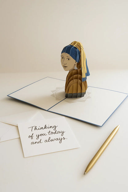 3D pop-up card with 'Girl with a Pearl Earring' design, a card with 'Thinking of you today and always', and a pen on a light surface.